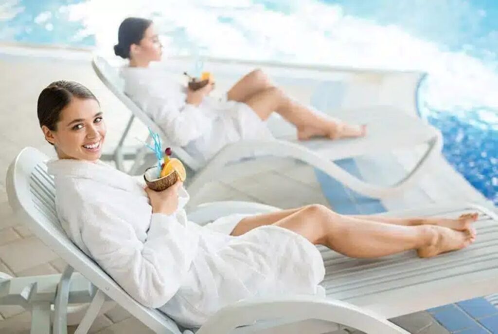 Two people relaxing in spa robes by a pool, representing a private sauna wellness session for stress relief and recovery in Willis, Texas