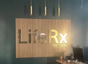 Gold LifeRx Wellness logo sign mounted on a modern wooden slat wall at the Willis, TX clinic reception desk.
